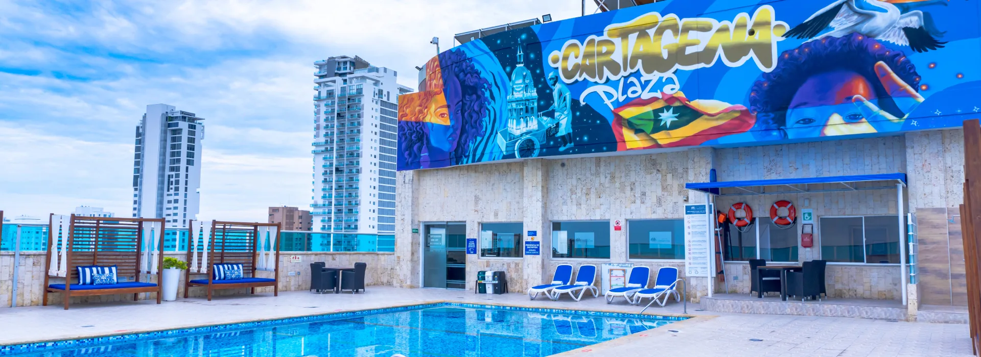 Piscina al aire libre con mural “Cartagena Plaza” y edificios al fondo