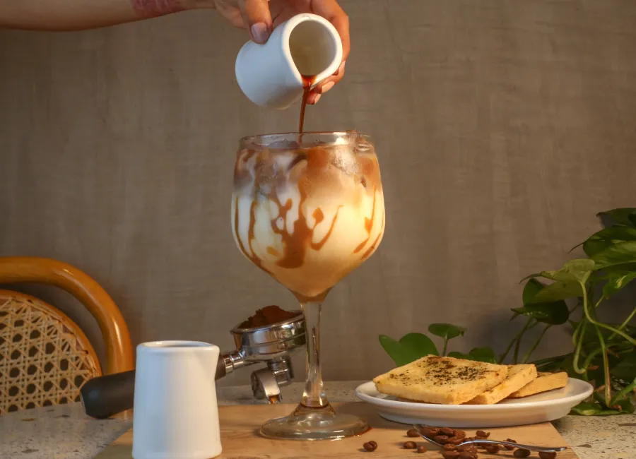 Sirviendo café en un recipiente con planta y galletas sobre mesa
