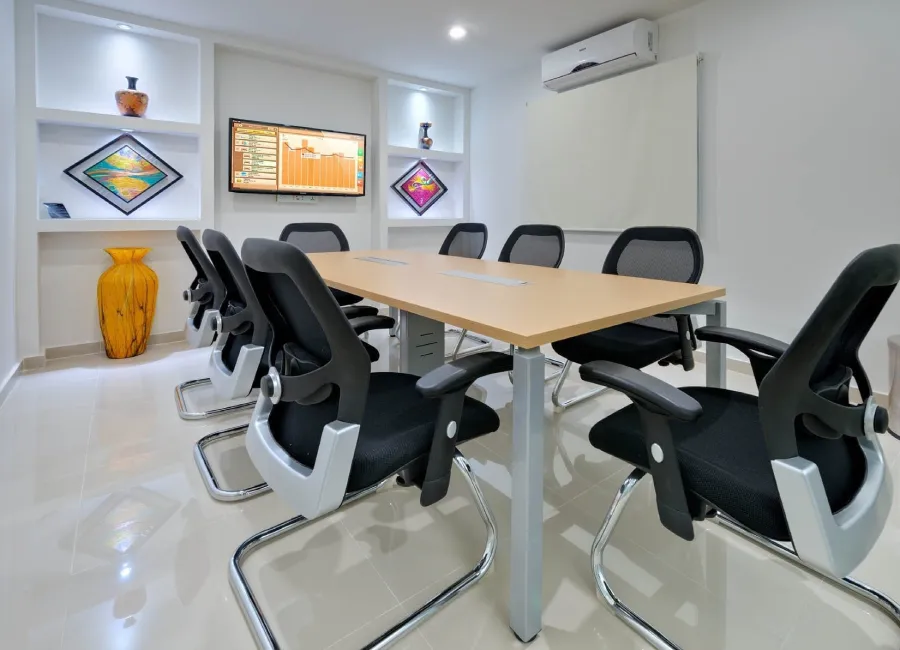 Sala de juntas moderna con mesas, sillas ergon&oacute;micas y paneles de TV.