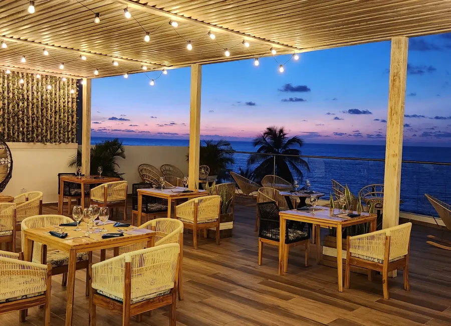 Terraza con mesas y sillas frente al mar al atardecer, con luces colgantes