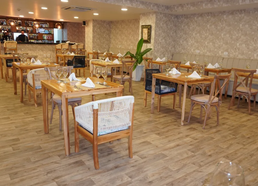 Comedor con mesas de madera y sillas, copas y decoración en el centro.