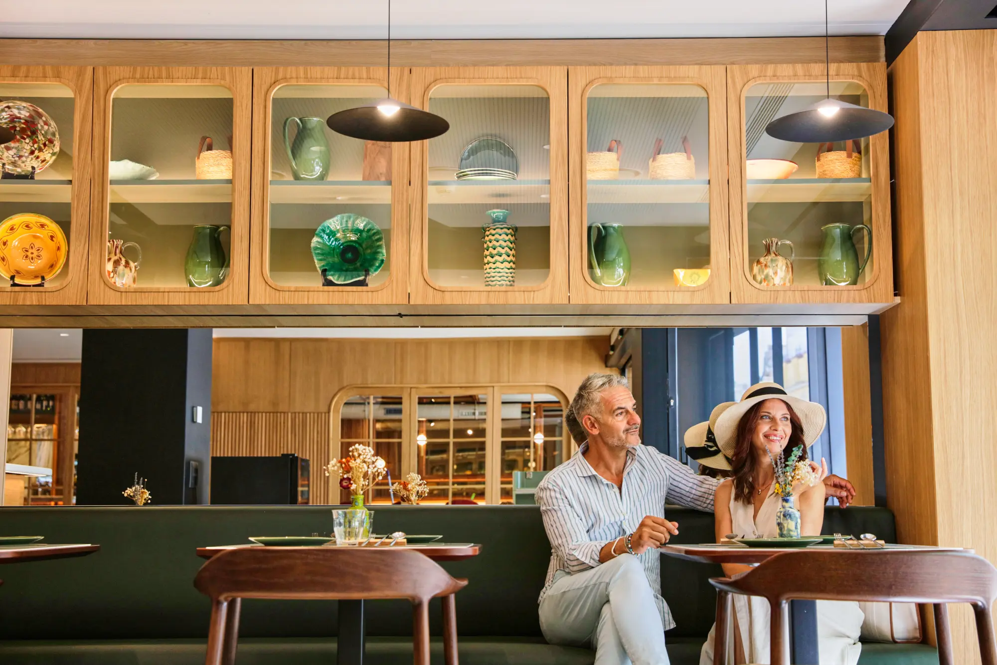 Dos personas sonríen en un acogedor restaurante decorado con cerámicas en vitrinas de madera.