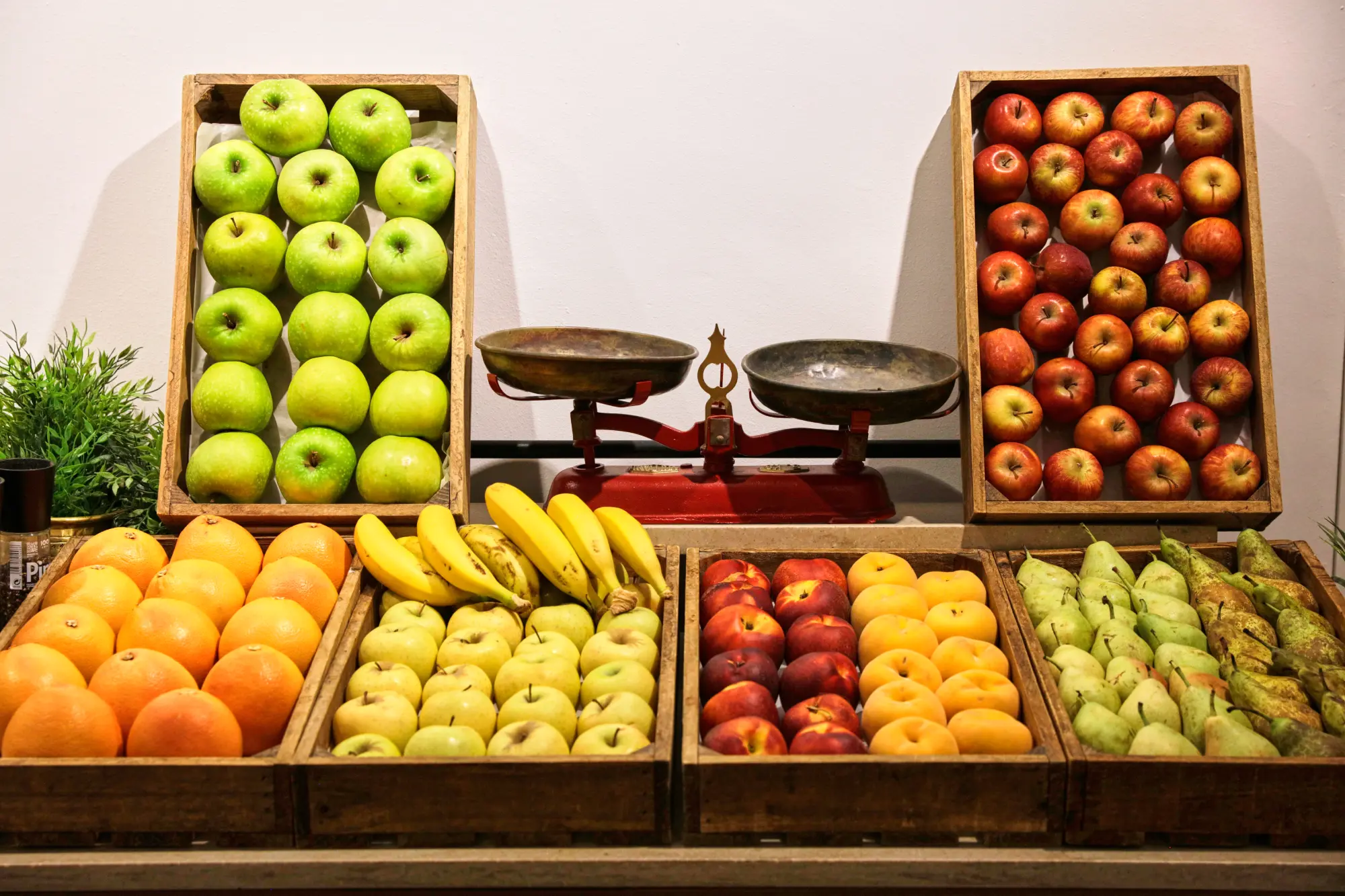 Frutas variadas en cajas: manzanas verdes y rojas, naranjas, plátanos, nectarinas y peras junto a una balanza.