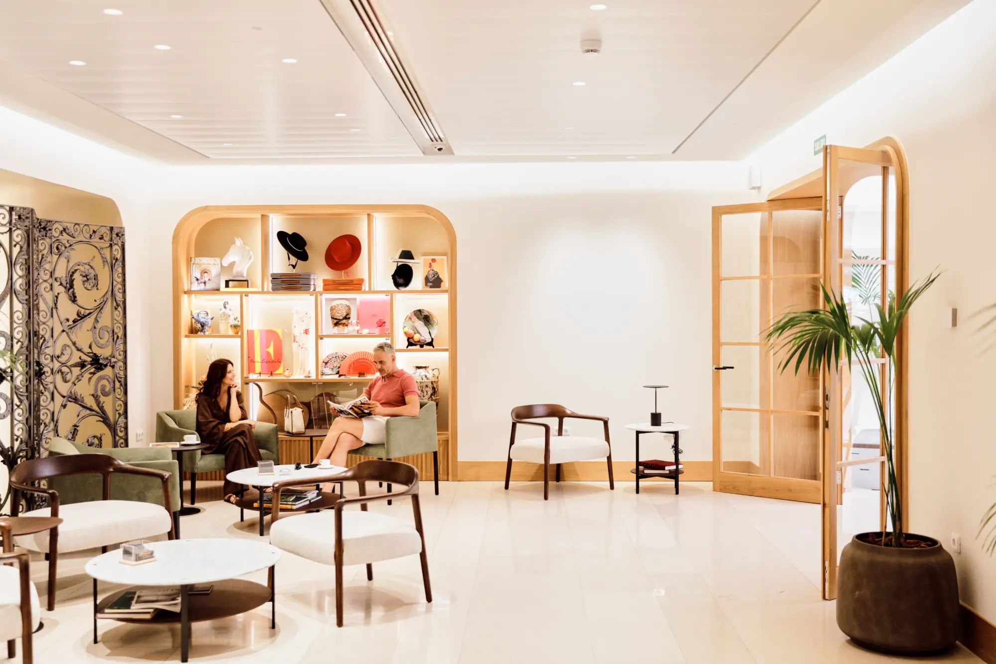 Sala moderna con muebles elegantes; dos personas conversan frente a estantes decorativos iluminados.