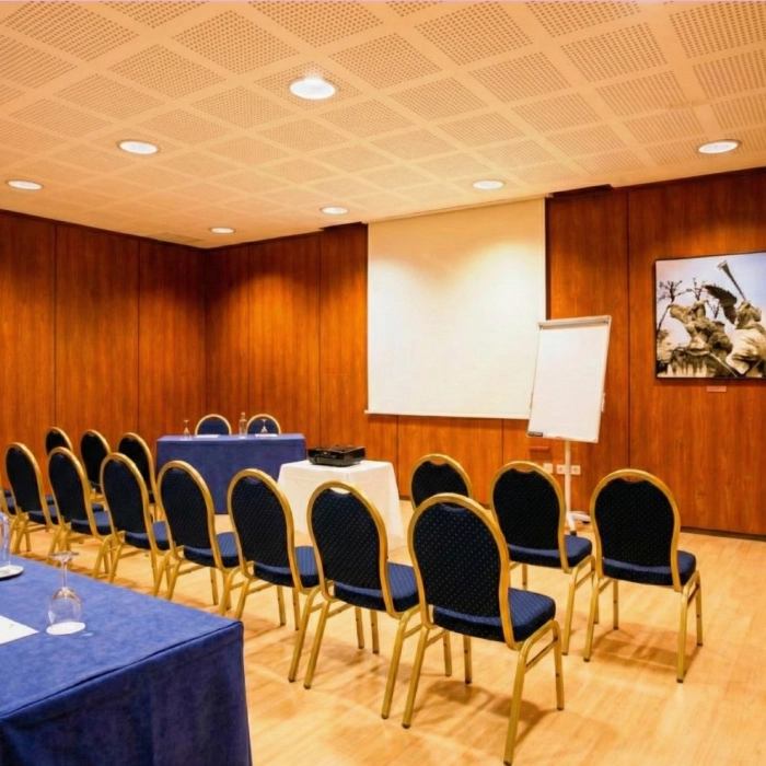 Sala de conferencias vac&iacute;a con sillas, proyector y pizarra blanca.