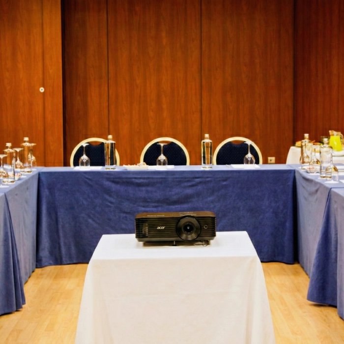 Proyector en mesa de reuniones con paredes de madera y botellas de agua.
