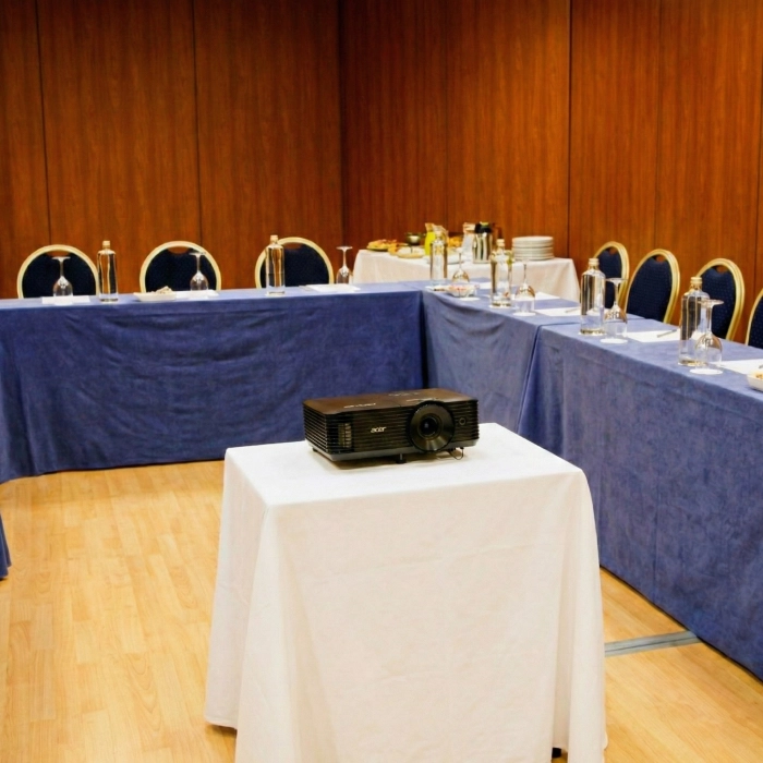 Sala de reuniones con proyector y mesas cubiertas con manteles azules.