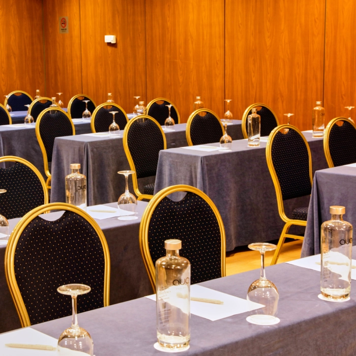 Sala de conferencias vac&iacute;a con mesas, botellas de agua y copas de cristal.