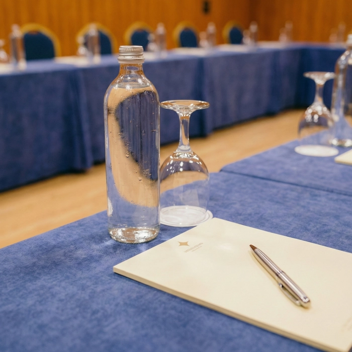 Botella, copa, cuaderno y bol&iacute;grafo sobre mesa azul en una conferencia.