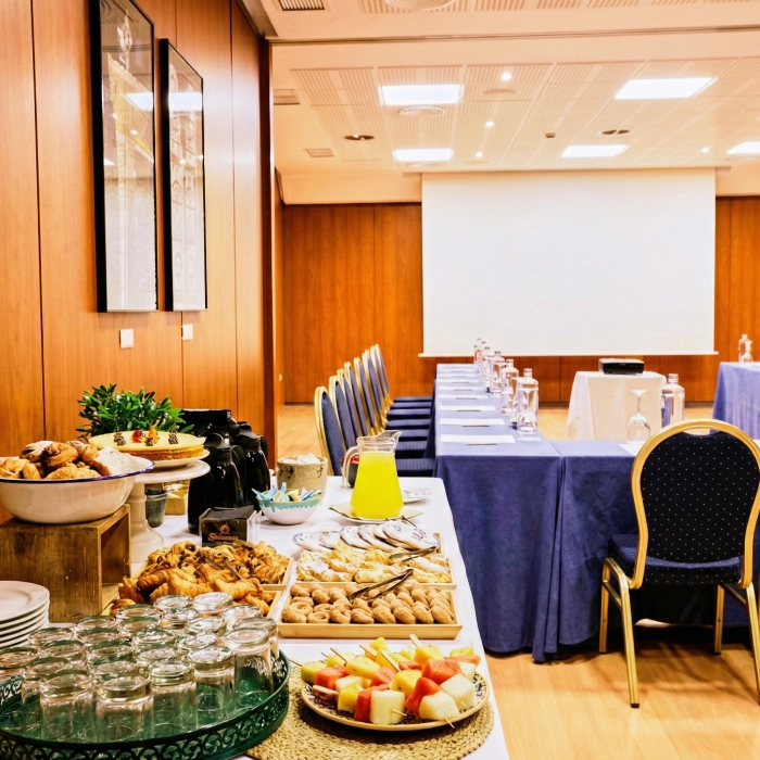 Sala de conferencia con mesas y un buf&eacute; de reposter&iacute;a y frutas.