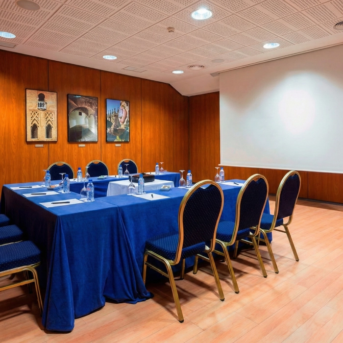 Sala de conferencias con mesa en U, sillas azules y proyector.