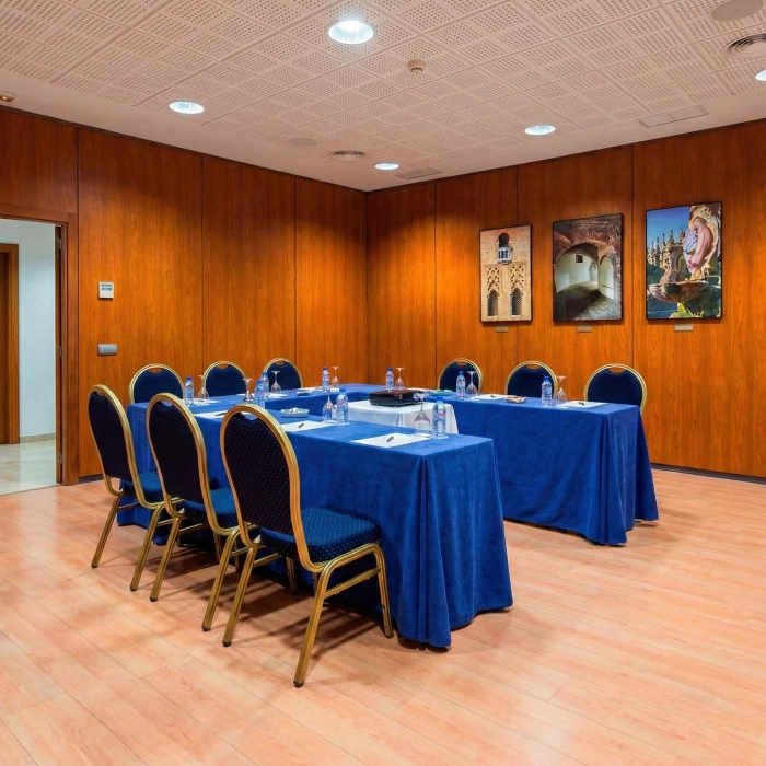Sala de reuniones con mesa azul, sillas y cuadros en la pared.