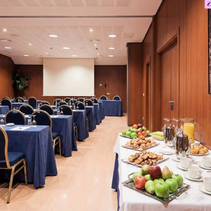 Sala de conferencias con mesas, sillas y mesa con frutas y bebidas.