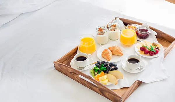Breakfast tray with fruit, croissants, coffee, juice, and yogurt on a bed.