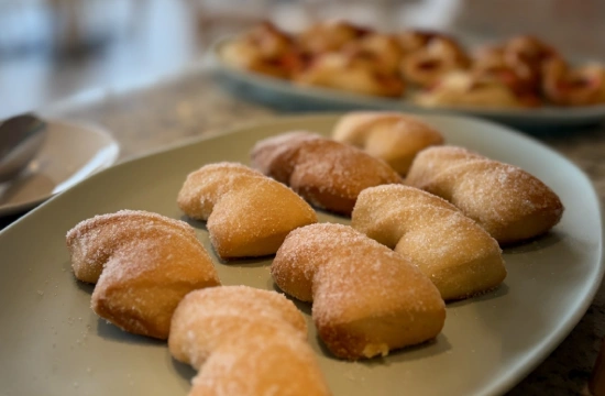 Croissants de az&uacute;car en un plato blanco con m&aacute;s postres al fondo.