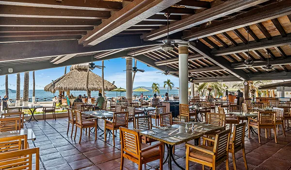 Outdoor beachside restaurant with wooden tables and chairs.