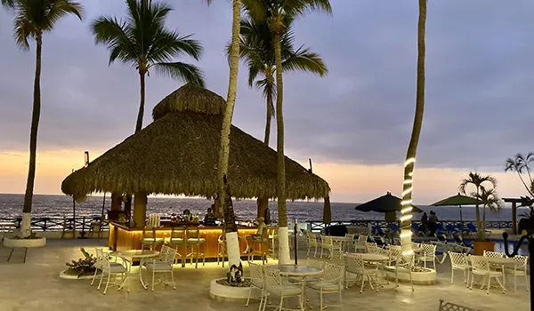 Beachside tiki bar at sunset with palm trees and empty tables.