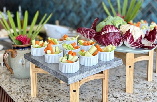 Mesa con verduras cortadas en cuencos blancos y hojas frescas al fondo.