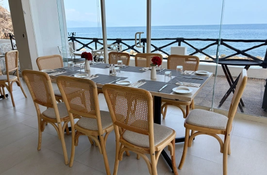 Mesa con sillas y vista al mar desde un comedor con grandes ventanales.