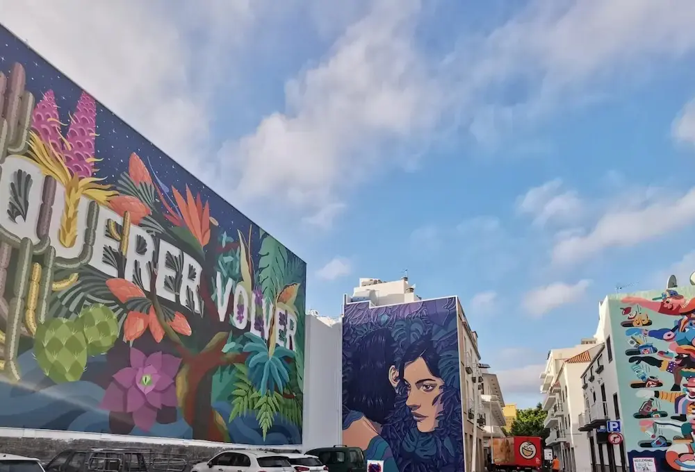 Murales coloridos en edificios bajo un cielo azul con nubes dispersas.