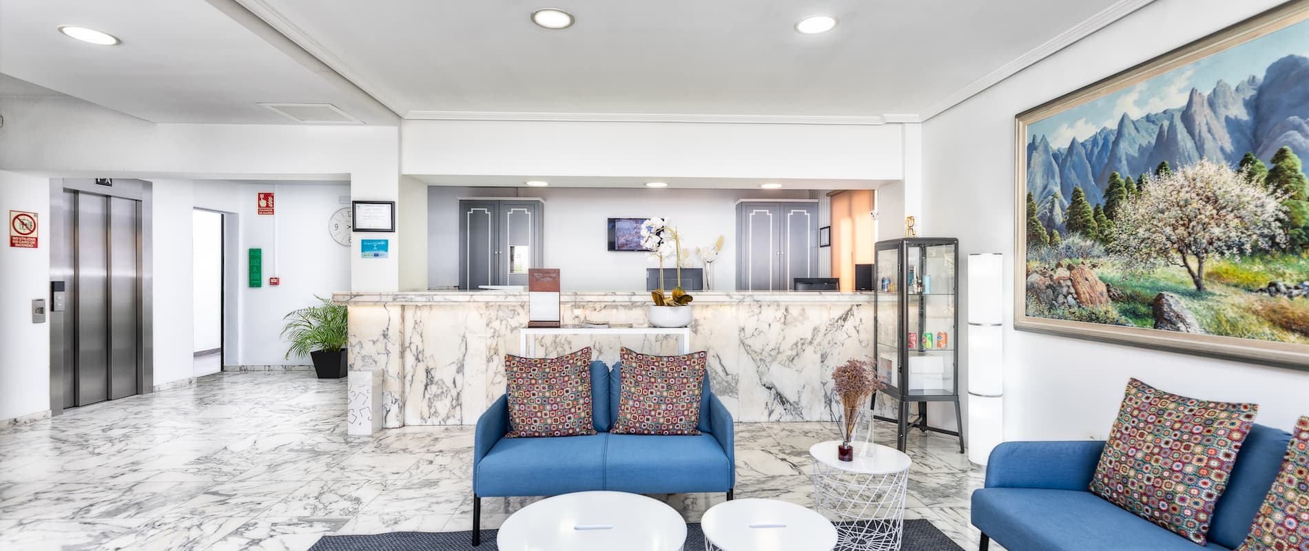 Recepción elegante de hotel, decoración en mármol, sofás azules y cuadro paisajístico en la pared.