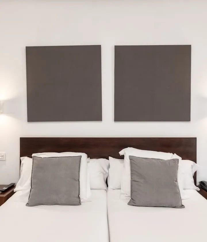Cama doble con cabecero oscuro, cojines grises y cuadros minimalistas sobre la pared.
