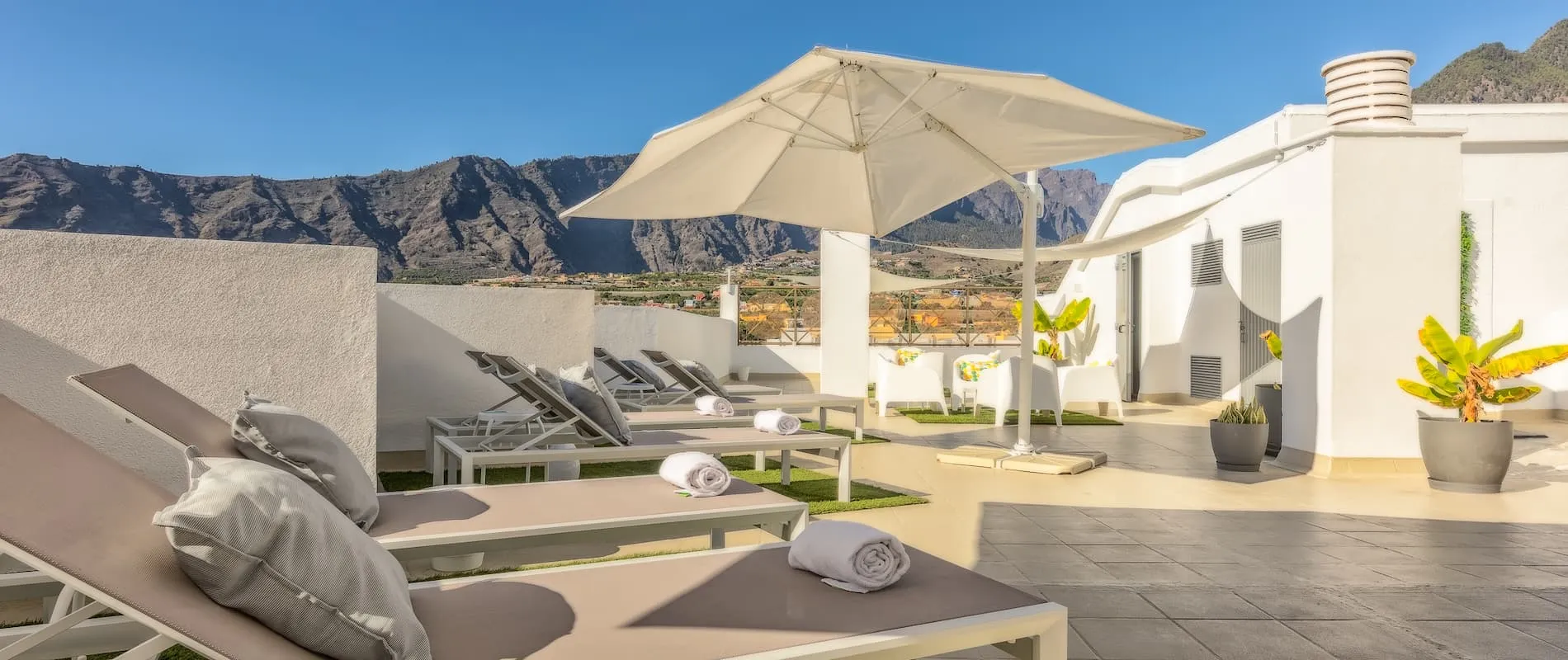 Terraza con tumbonas, sombrilla, montañas al fondo y cielo despejado.