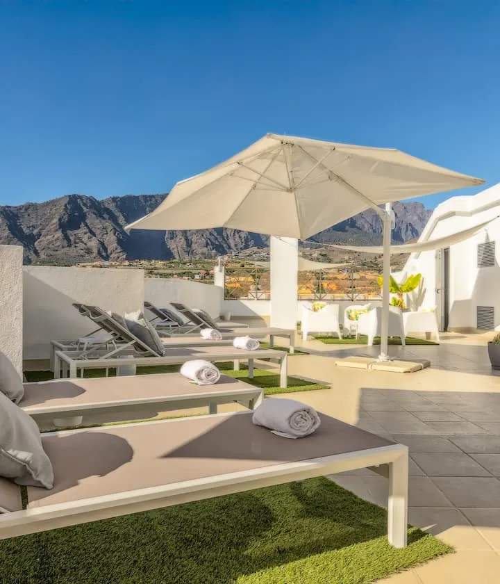 Terraza con tumbonas y sombrilla, vistas a montañas bajo un cielo despejado.