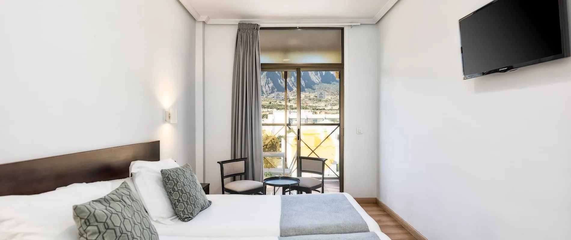 Habitación de hotel con cama doble, televisor y balcón con vista a las montañas.
