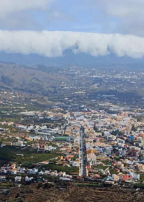 Vista panorámica de una ciudad con montañas y nubes al fondo.