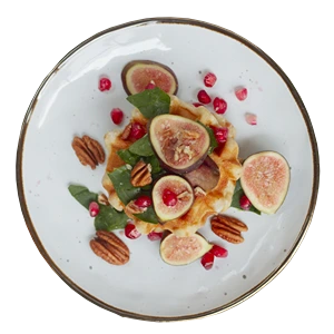 Waffle with fresh figs, pomegranate seeds, spinach, and pecans on a white plate.