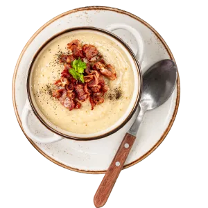 Bowl of creamy soup topped with crispy bacon and herbs, served with a spoon on a plate.