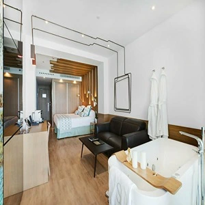 Modern hotel room with bed, couch, freestanding bathtub, and stylish decor.