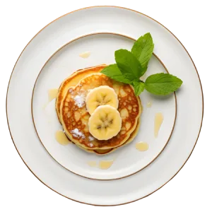 Pancakes with banana slices, syrup, and mint leaves on a white plate.