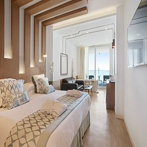 Modern hotel room with large bed, elegant decor, and ocean view through a window.
