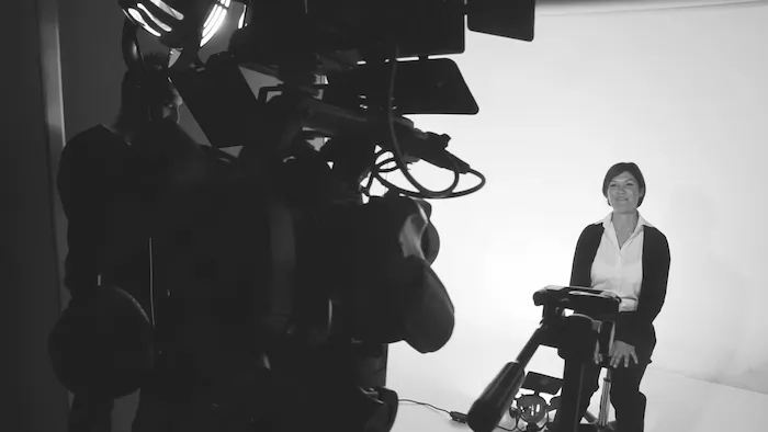 Person sitting, facing a camera setup in a studio.