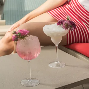 Two floral cocktails on a table beside a person in a striped skirt.