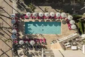 Aerial view of a pool with red loungers and white umbrellas around it.