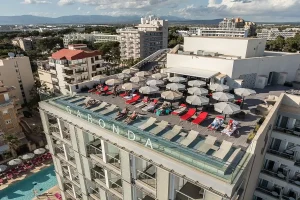 Rooftop terrace with people sunbathing and umbrellas at a hotel in a city.