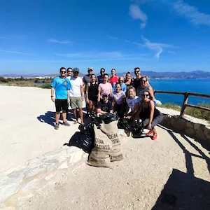 Group of people posing with bags of trash by the ocean on a sunny day.