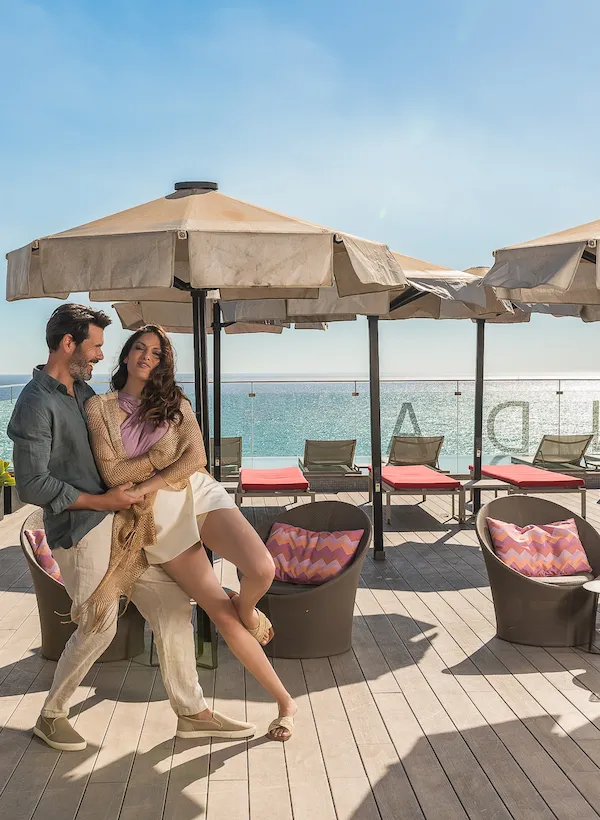 A couple dancing on a deck with umbrellas and an ocean view in the background.
