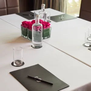 Conference setup with water, glasses, notepads, pink flowers on a table with white cloth.