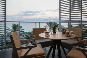 Table with champagne, candles, and snacks on a balcony overlooking the ocean at sunset.