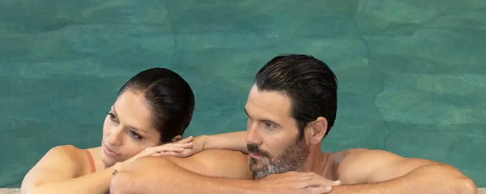 Couple relaxing in a pool, leaning on the edge, with turquoise water in the background.