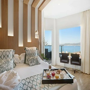 Bright hotel room with ocean view, modern decor, and breakfast tray on the bed.
