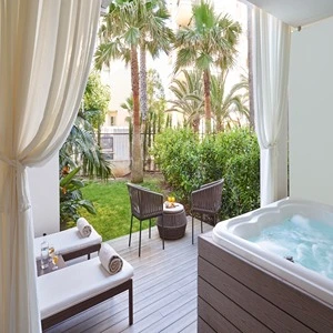 Outdoor patio with hot tub, loungers, and chairs, surrounded by greenery and palm trees.