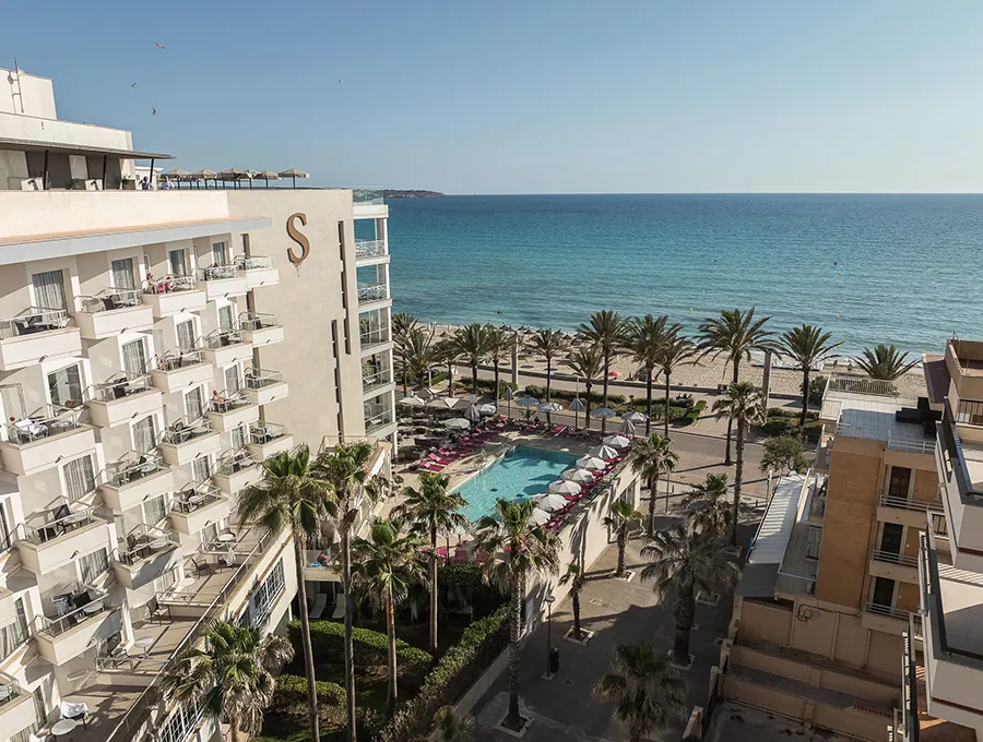 Beachfront hotel with pool, palm trees, and ocean view under a clear blue sky.