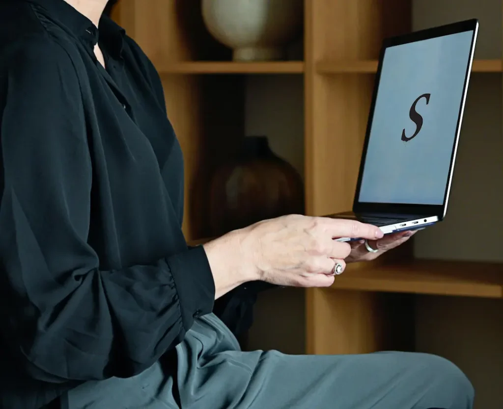 Person holds a laptop with the letter "S" on screen.