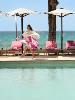 Woman by pool with umbrellas and ocean in background.