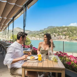 Two people dining on a terrace with a scenic view of the ocean and mountains.